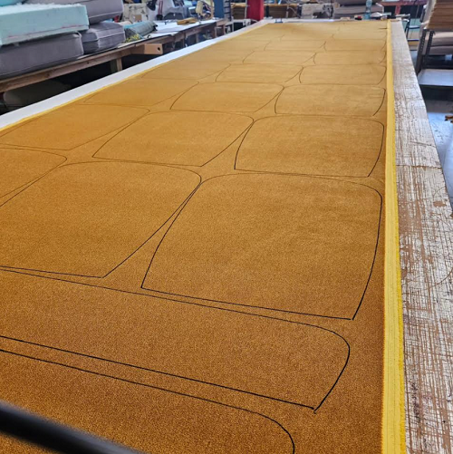 Mustard colored upholstery fabric laid out on a table and marked for cutting